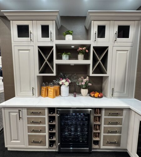 Korner kitchen cabinetry display at KBIS 2025 featuring elegant beige cabinets with built-in wine storage, marble countertop, and floral decor.